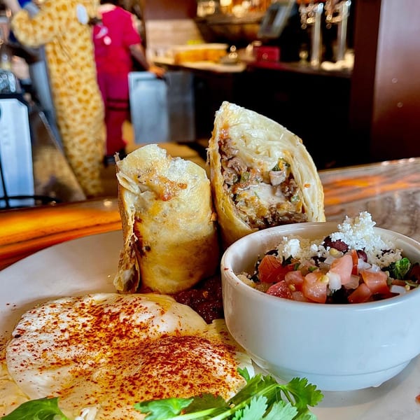Two crispy burritos, two fried eggs with paprika, and a side of salsa on a white plate.