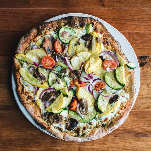 Unwined Kitchen & Bar's New American pizza, topped with zucchini, squash, mushrooms, tomatoes, and red onion.