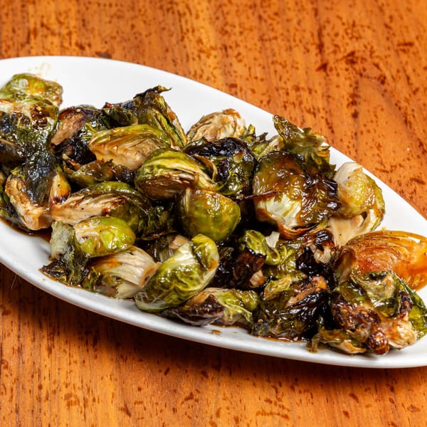 A white platter filled with glistening, roasted Brussels sprouts on a wooden table.