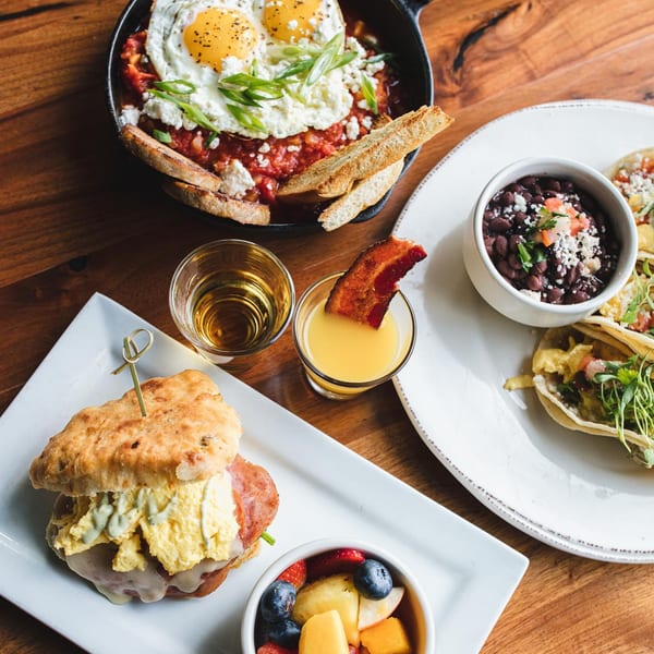 Unwined Kitchen & Bar's brunch spread with shakshuka, breakfast tacos, biscuit sandwich, and fruit.