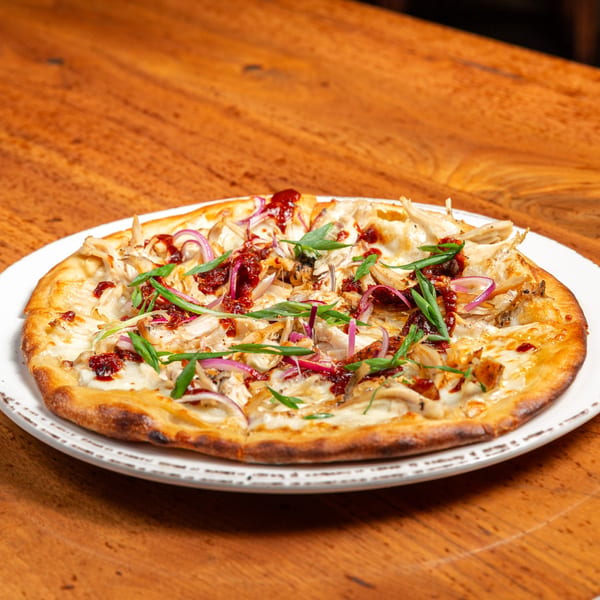 Unwined Kitchen & Bar's New American pizza with chicken, red onions, and green onions on a wooden table.