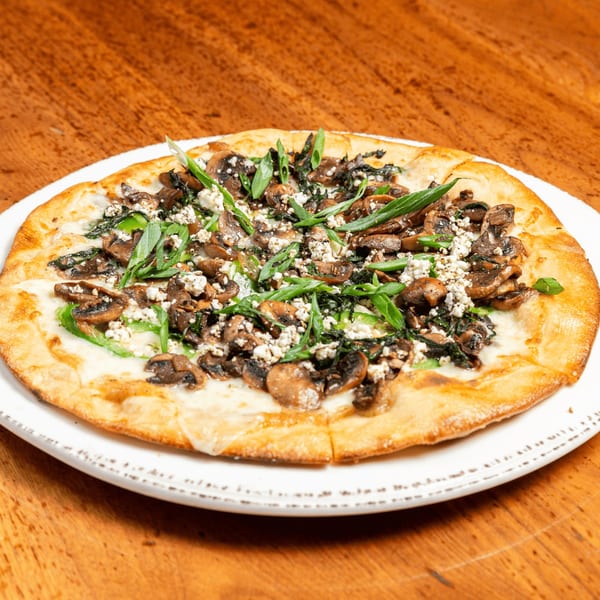 Mushroom and spinach flatbread pizza with crumbled feta and green onions on a white plate.