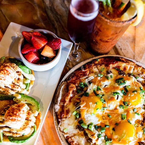 Unwined Kitchen & Bar's breakfast pizza with eggs, avocado toast, fruit, and two drinks.