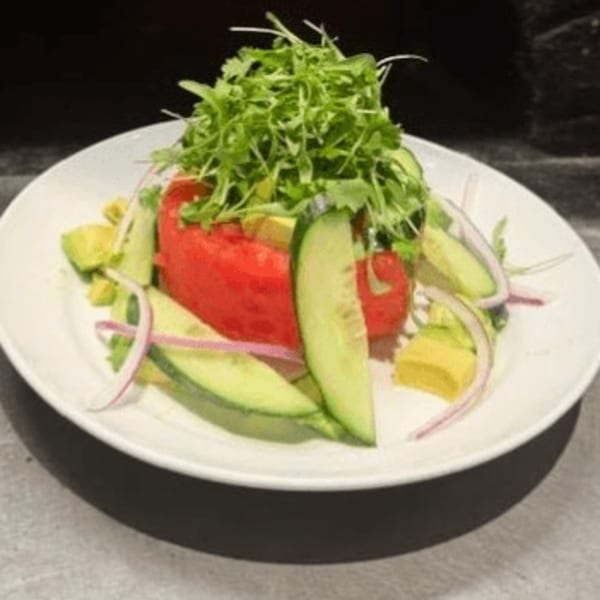 A fresh salad with a large red tomato, avocado, cucumber slices, red onion, and arugula.