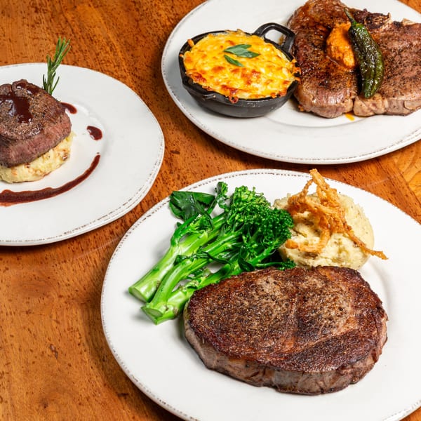 Three plates of New American cuisine, including steaks, mac and cheese, mashed potatoes, and broccolini.