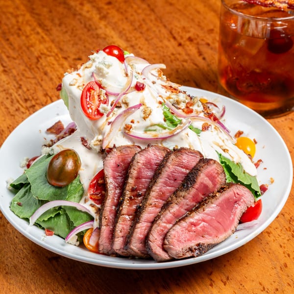 Unwined Kitchen & Bar's steak salad with blue cheese, tomatoes, onions, bacon, and a cocktail.
