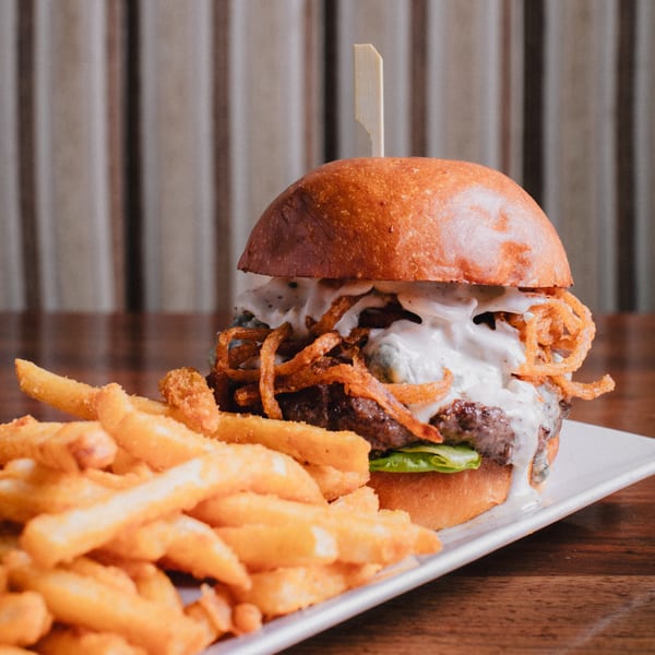A New-American burger with crispy onions and creamy sauce, served with golden french fries.
