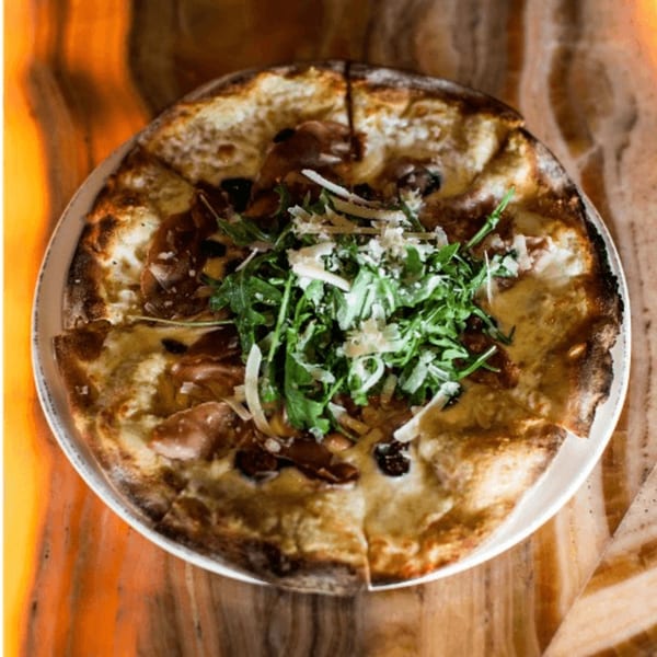 A whole pizza with prosciutto, arugula, and shaved parmesan cheese on a white plate.