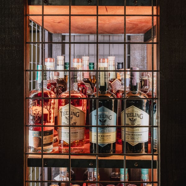 A metal-caged shelf displays various bottles of Teeling Irish Whiskey, illuminated by warm orange light.