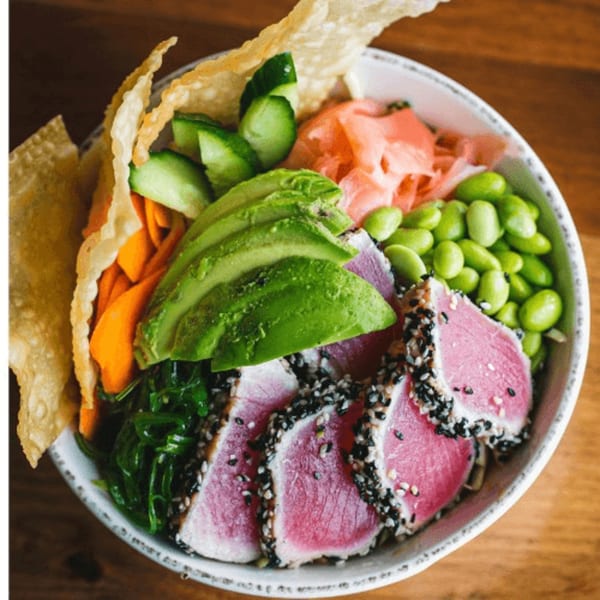 Seared tuna poke bowl with avocado, edamame, pickled ginger, carrots, seaweed, and wonton crisps.