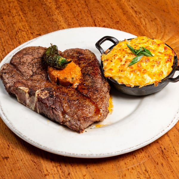 Grilled steak with a dollop of butter and a side of baked macaroni and cheese.