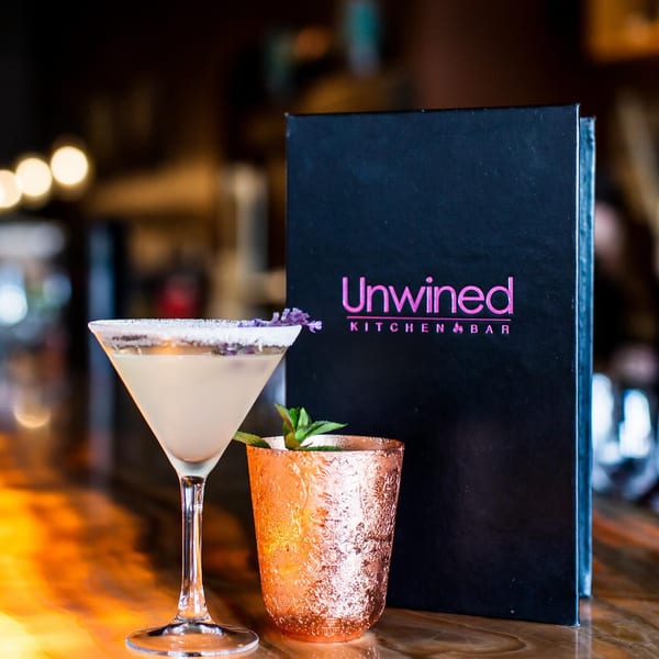 A martini and a copper mug with mint sit next to an Unwined Kitchen & Bar menu.