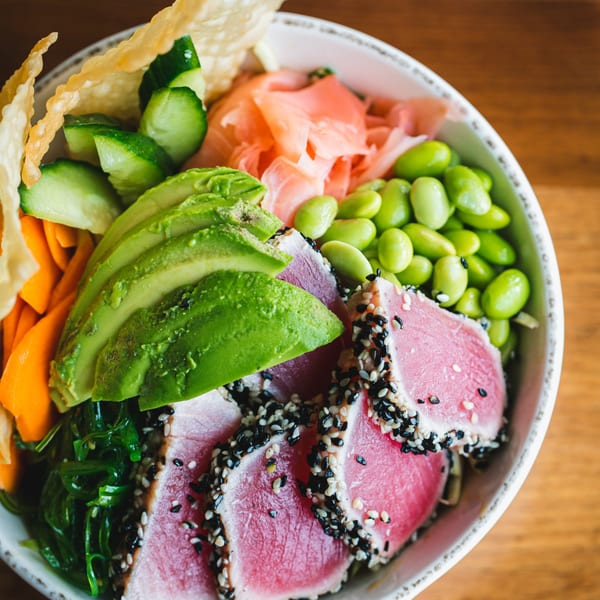 Close-up of a vibrant New American poke bowl with seared tuna, avocado, edamame, and pickled ginger.