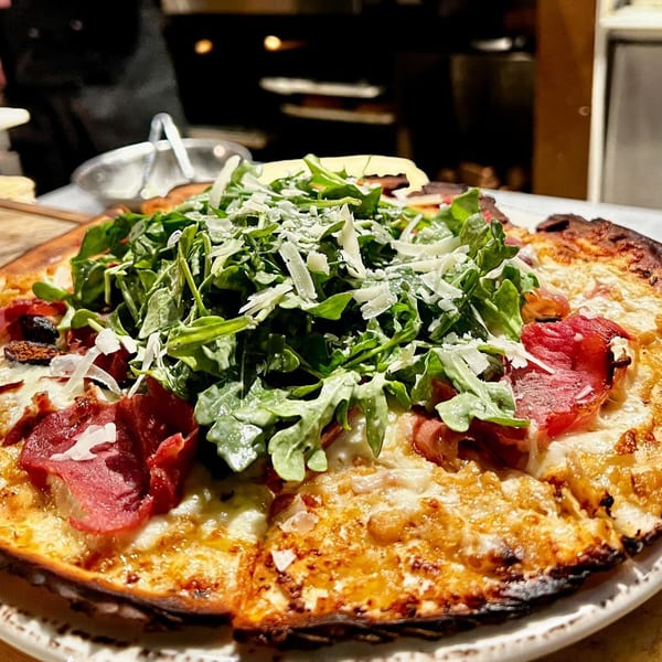 A New American pizza topped with arugula, shaved cheese, and cured meats.