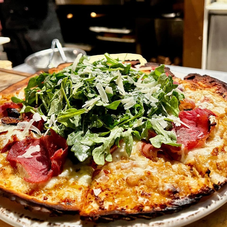 A New American pizza topped with arugula, shaved cheese, and cured meats.
