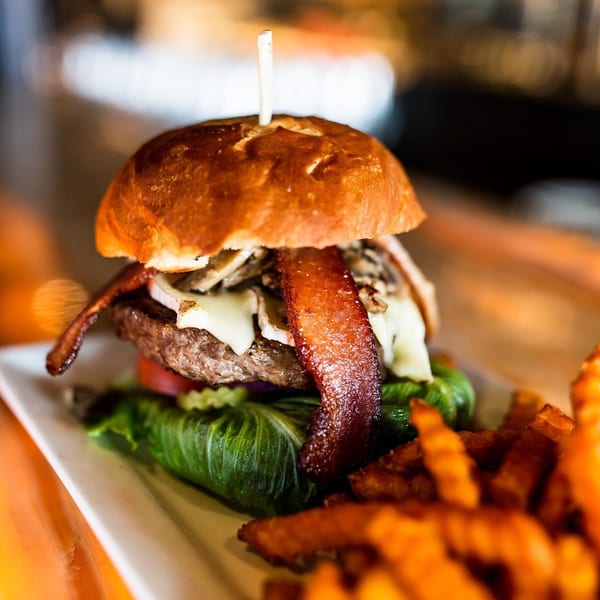 Unwined Kitchen & Bar's New American burger with bacon, mushrooms, cheese, lettuce, and fries.