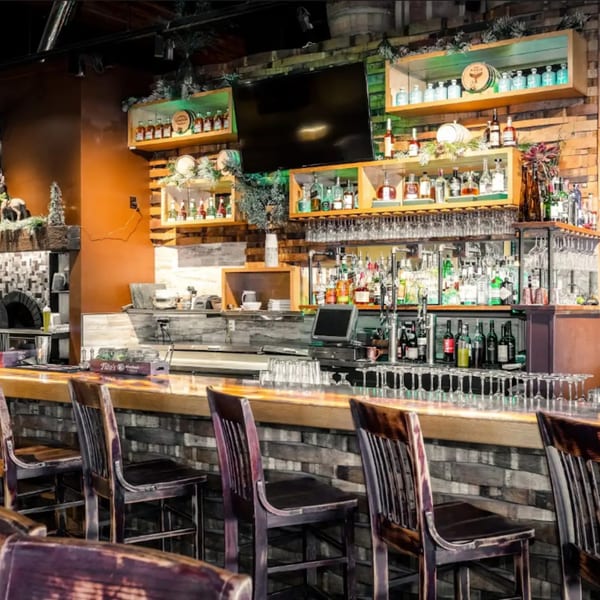 Unwined Kitchen & Bar's well-stocked bar area with bottles, glasses, and bar stools.
