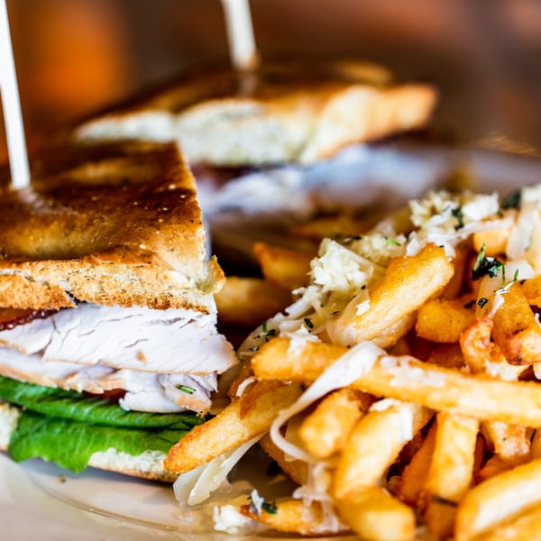 Unwined Kitchen & Bar's turkey sandwich with lettuce and fries topped with cheese and herbs.