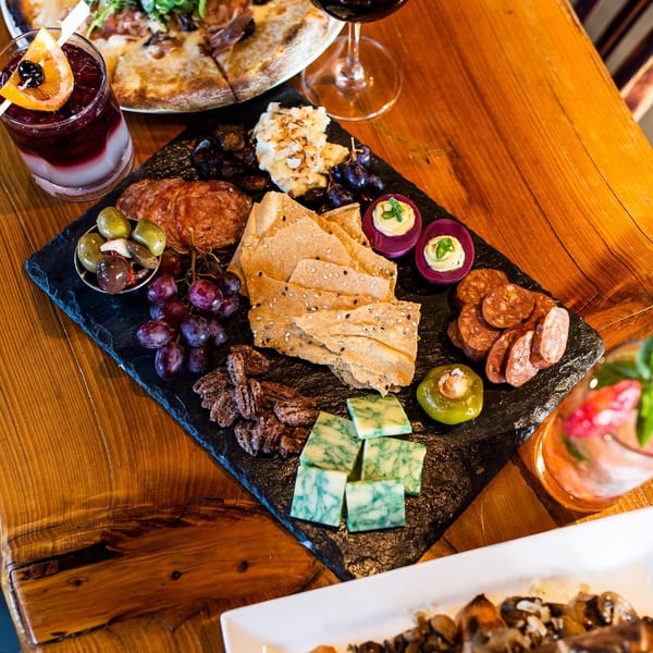 A slate charcuterie board with meats, cheeses, grapes, olives, crackers, and deviled eggs.