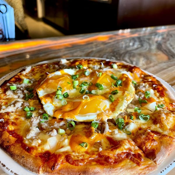 Unwined Kitchen & Bar's breakfast pizza topped with sausage, cheese, two fried eggs, and scallions.